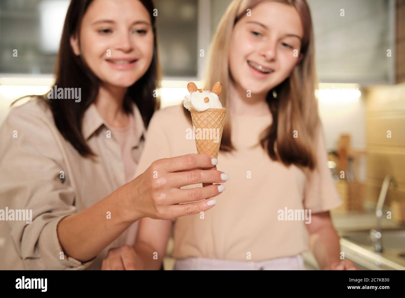 Glückliche junge Frau zeigt leckere hausgemachte Eis in Waffelkegel von ihrer Teenager-Tochter mit Mandelnüssen dekoriert Stockfoto