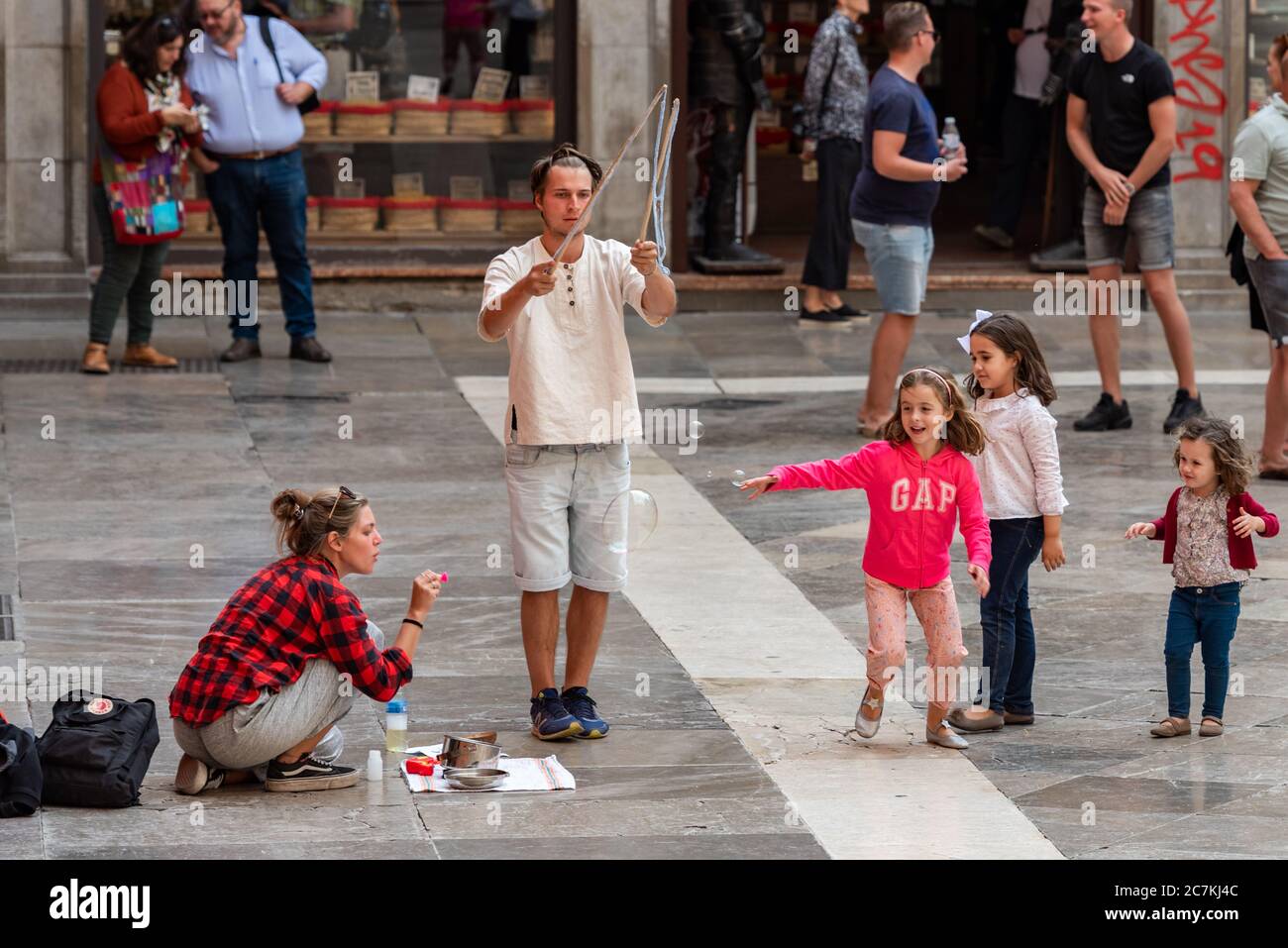 Kinder jagen Blasen von zwei Straßenkünstlern auf der Plaza de Las Pasiegas, Granada. Stockfoto