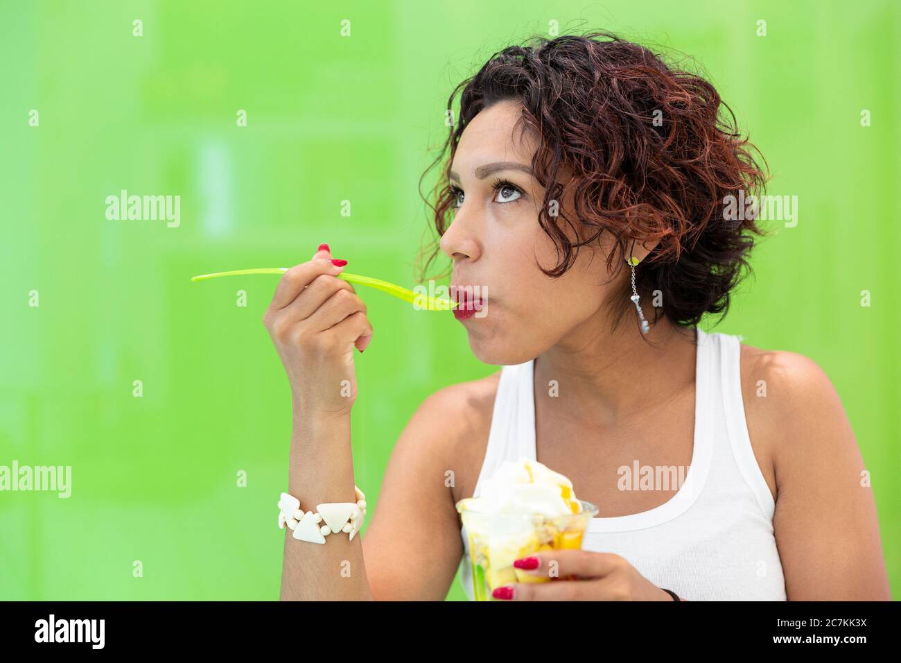 Nahaufnahme eines Mädchens mit brauner Haut, das auf grünem Hintergrund ein Eis isst. Leerzeichen für Text. Selektiver Fokus. Sommer und gesundes Lifestyle-Konzept. Stockfoto
