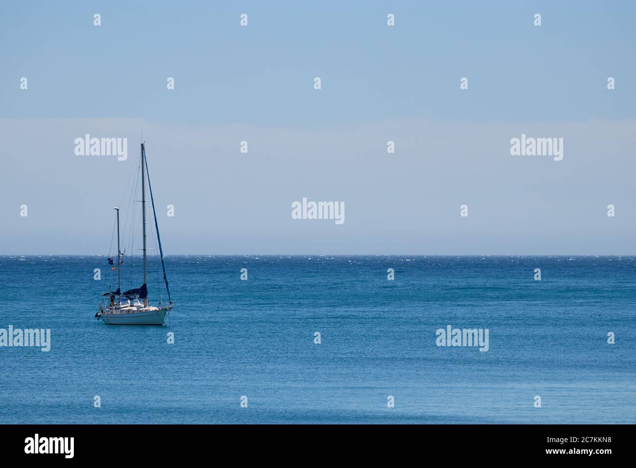 Horizontale Aufnahme mit einem Segelboot links vom Rahmen auf einem ruhigen Meer mit einem hellblauen wolkenlosen Himmel in malaga Stockfoto