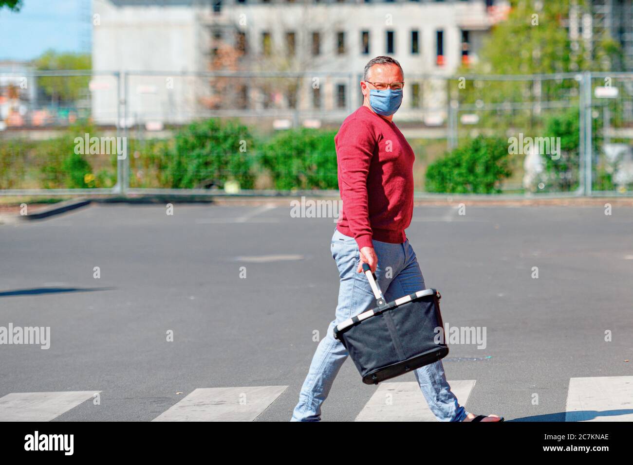 Mann mit Mund-Nase-Schutz wegen der Coronakrise auf dem Weg zum Supermarkt mit einem Warenkorb Stockfoto