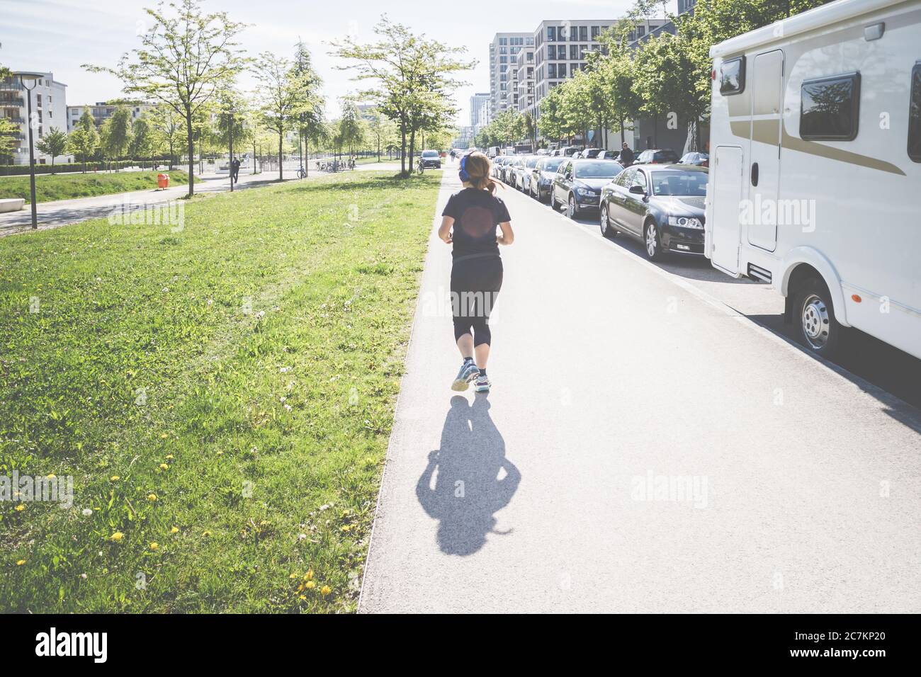 Rückansicht einer jungen Frau mit Kopfhörern, sie joggt durch München, lebt, lebt und arbeitet in der bayerischen Landeshauptstadt an der Isar. Stockfoto