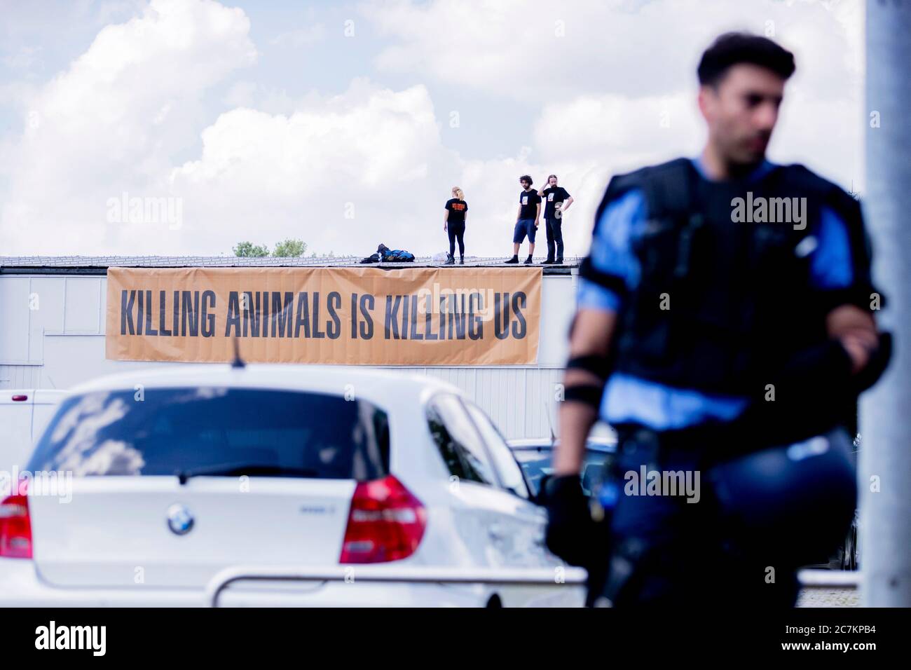 18. Juli 2020, Brandenburg, Königs Wusterhausen: Tierschutzaktivisten stehen während einer Blockade des Schlachthofs hinter einem Polizisten auf dem Dach des Wiesenhof in Niederlehme bei Königs Wusterhausen. Ein Banner lautet: "Tiere töten tötet uns". Quelle: dpa picture Alliance/Alamy Live News Stockfoto