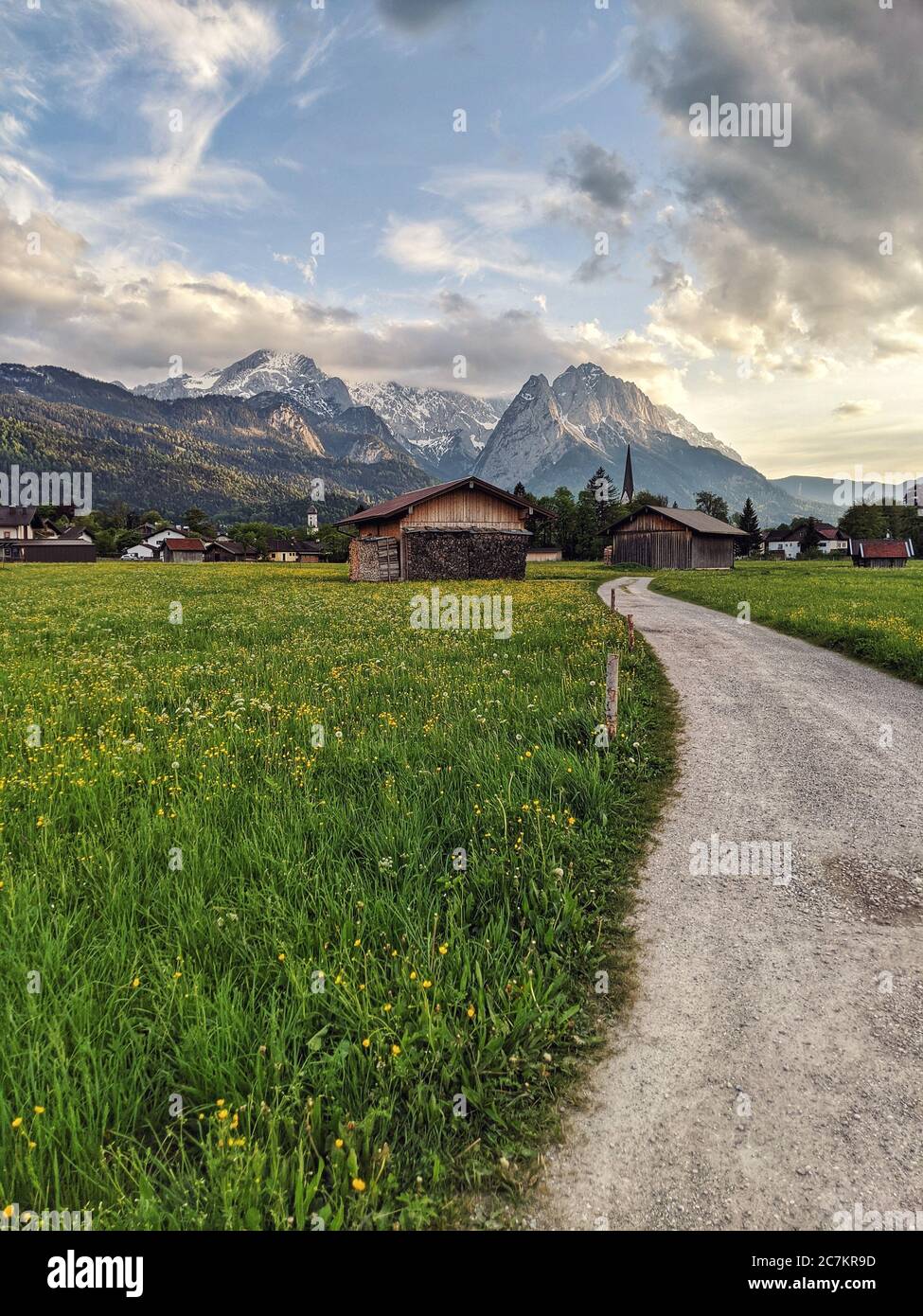 Weg führt entlang einer Frühlingswiese mit Blick auf das Zugspitzmassiv und 2 Kirchtürme in Garmisch-Partenkirchen Stockfoto