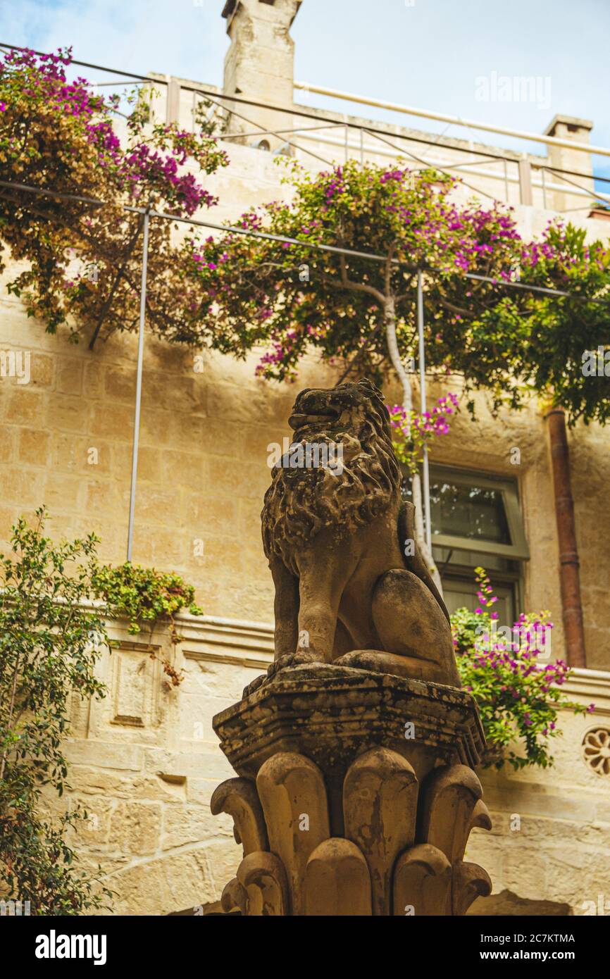 Statue eines Tieres vor einem alten Stein Gebäude mit Blumen und Pflanzen dekoriert Stockfoto