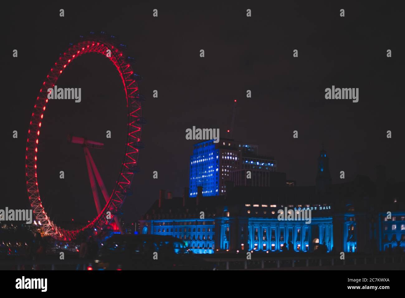 Weitwinkelaufnahme des roten London Eye nebenan Ein Gebäude in der Nacht Stockfoto