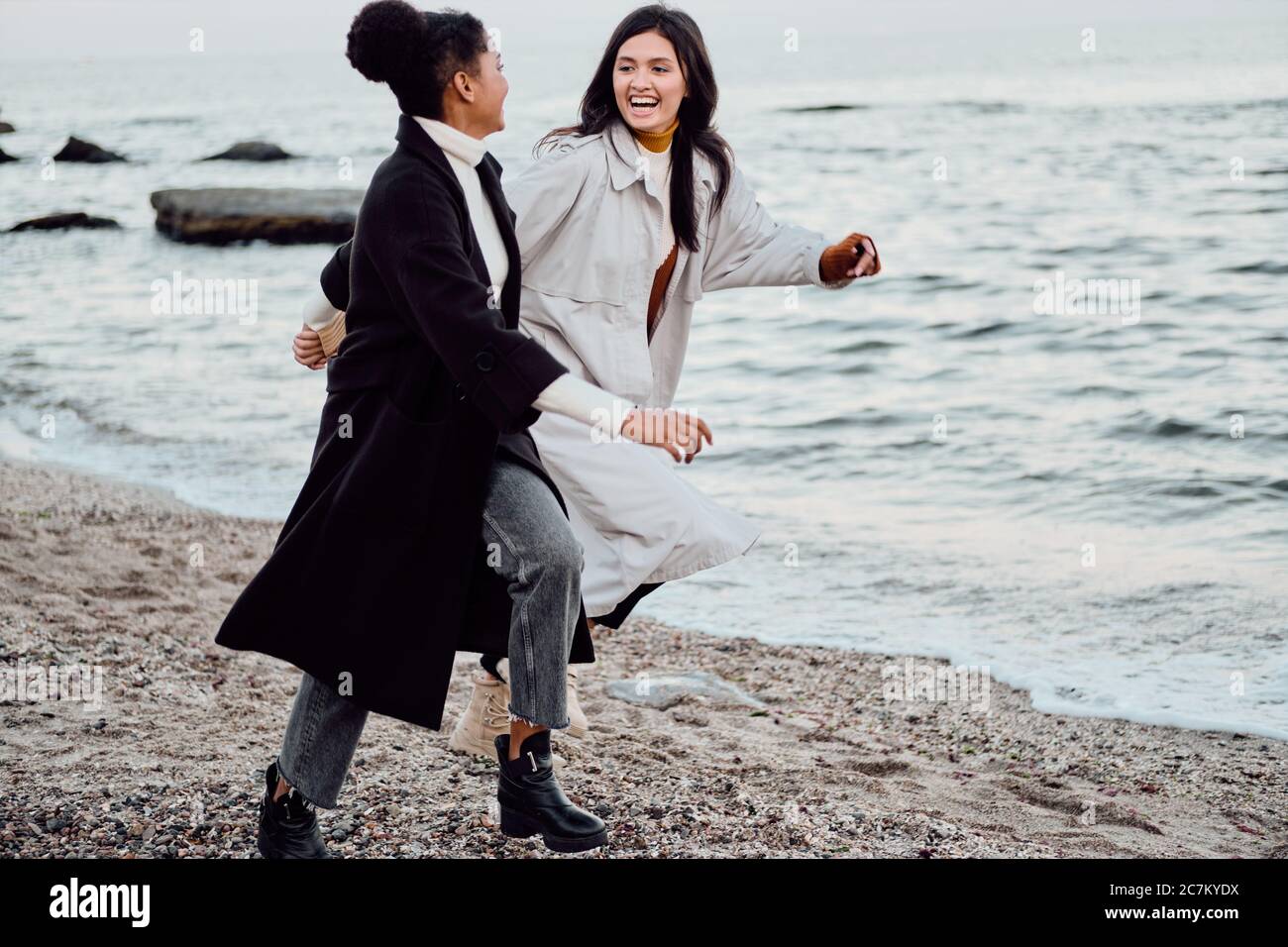 Zwei schöne Mädchen in Trenchcoats glücklich am Meer laufen Stockfoto