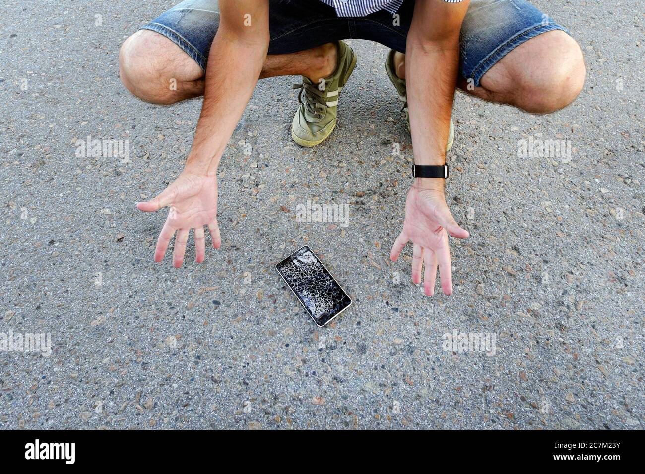 Guy ließ sein Handy auf den Asphalt fallen und brach es. Ein frustrierter Mann mit einem defekten Handy. Mann sitzt und hält ein defektes Smartphone Stockfoto