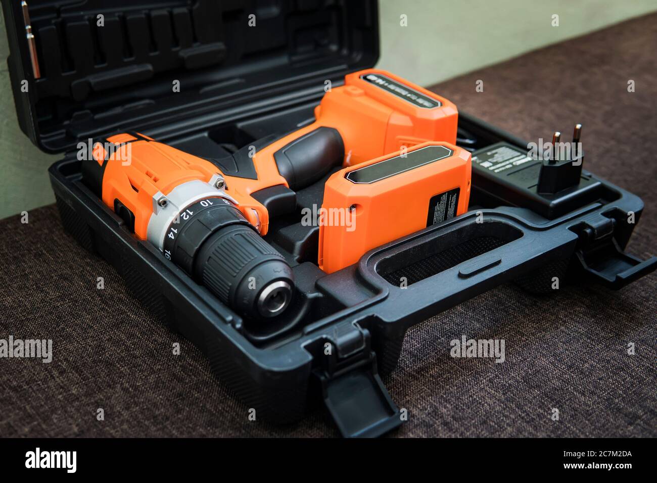 Akku-Bohrmaschine orange mit schwarzem Akku. Orangefarbener Schraubendreher oder Bohrer in einem schwarzen Behälter liegt auf dem Boden. Werkzeug zum Anziehen von Schrauben. Schraubpistole Stockfoto