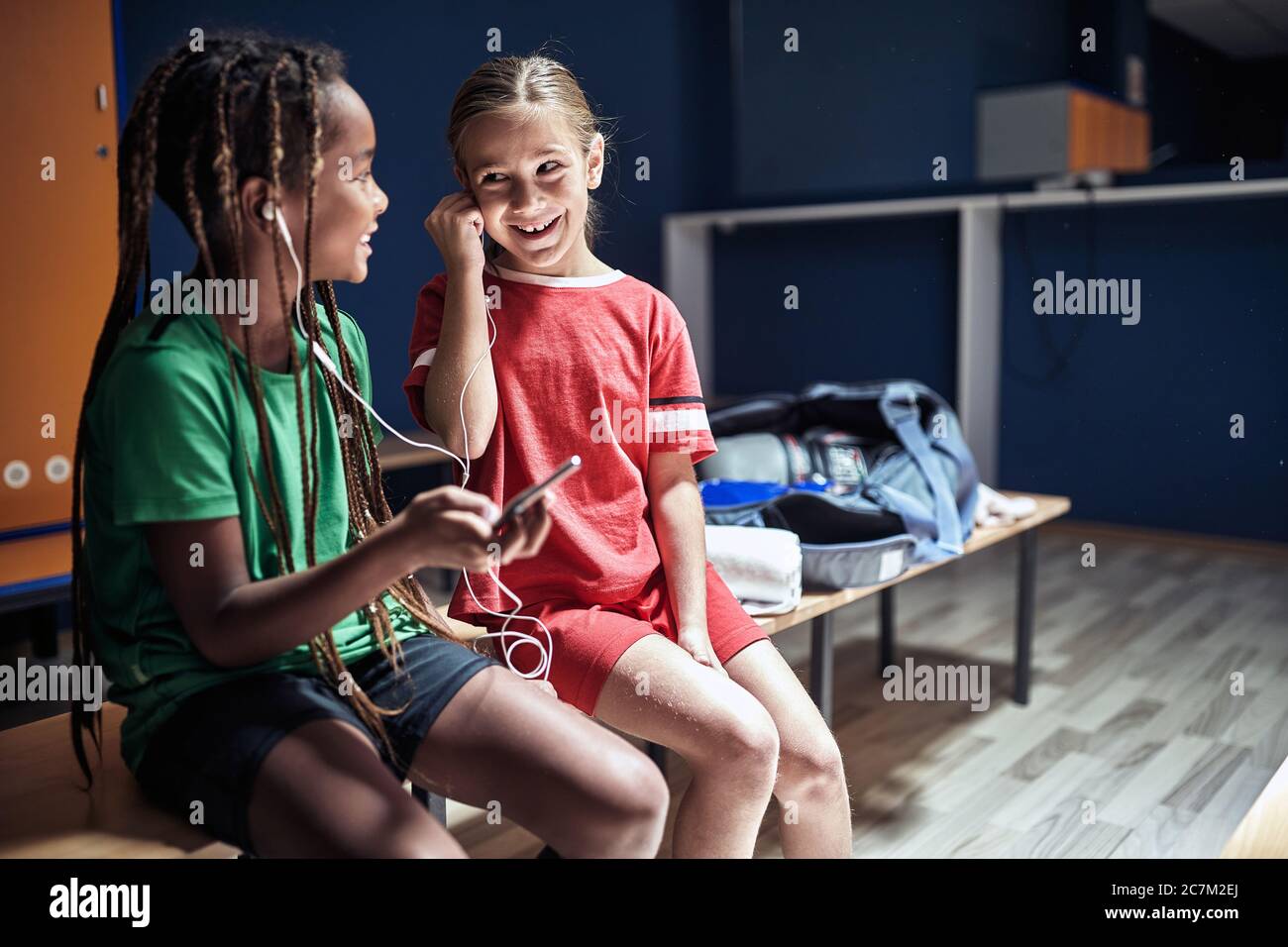 Lächelnde Freunde Kinder vor dem Training hören Musik am Telefon in der Umkleidekabine. Stockfoto