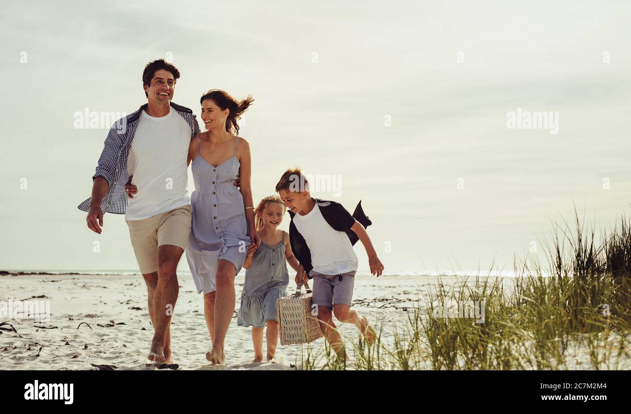 Familie zu Fuß am Strand mit Kindern mit Picknickkorb. Schöne Familie am Strand an einem Sommerwochenende. Stockfoto