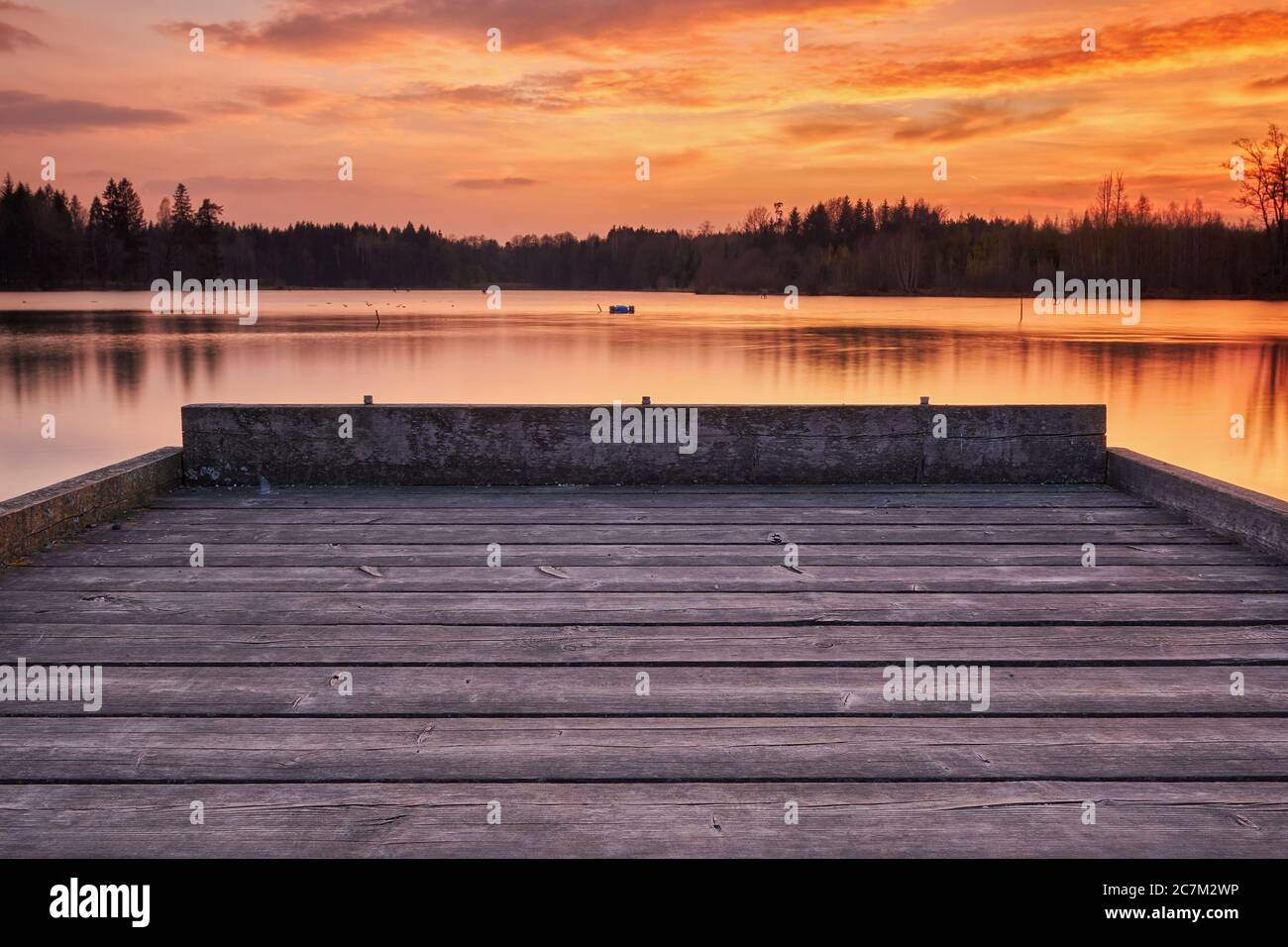 Ein kleines Dock an einem kleinen See in Österreich bei Sonnenuntergang. Der Himmel und das Wasser sind von der Sonne gefärbt. Stockfoto