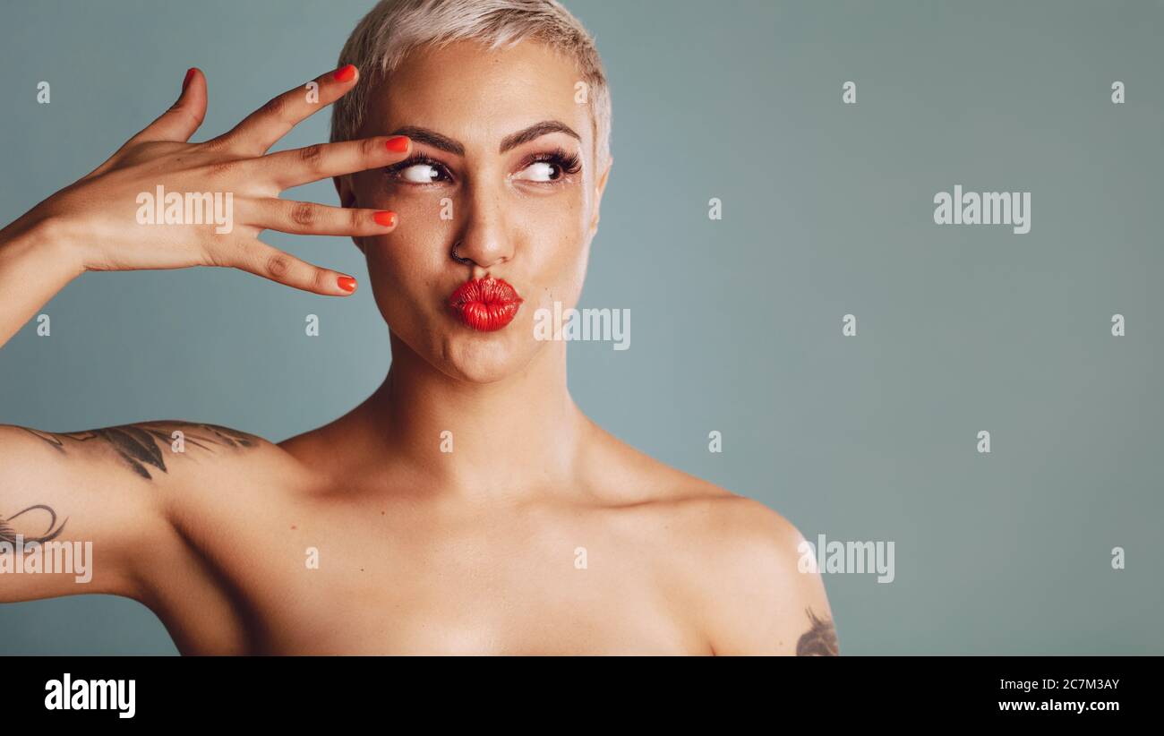 Trendy weibliche Modell mit Make-up suchen seitlich mit puckering Lippen. Schöne Frau mit kurzen blonden Haaren vor grauem Hintergrund. Stockfoto