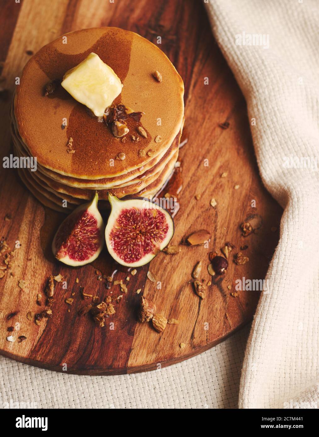 Vertikale Aufnahme von Pfannkuchen mit Sirup, Butter, Feigen und gerösteten Nüssen auf einem Holzteller Stockfoto