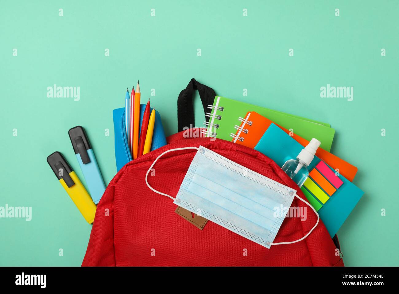 Schulbedarf mit medizinischer Maske und Desinfektionsmittel auf minzem Hintergrund Stockfoto