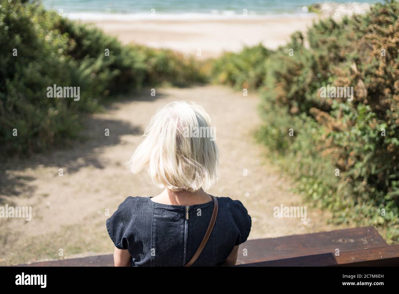 Frau sitzt auf einer Bank auf einem Klippenweg Spaziergang mit Blick auf das Meer Stockfoto