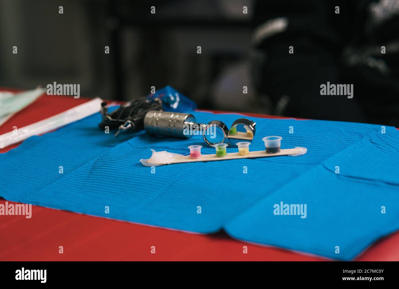 Foto von Tätowiermaschine und Tintenbehälter auf einem blauen Stoff Stockfoto
