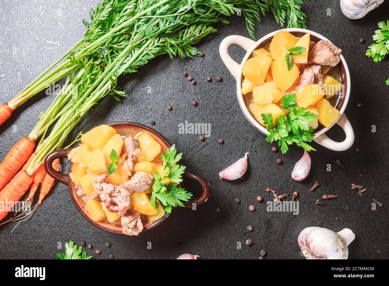 Kartoffelschmorbraten, gebacken mit Fleisch, Schweinefleisch und Petersilie auf einem tiefen Teller neben einem Gewürz numerisch Karotte auf einem schwarzen Tisch. Flach legen, Kopierraum, Draufsicht Stockfoto
