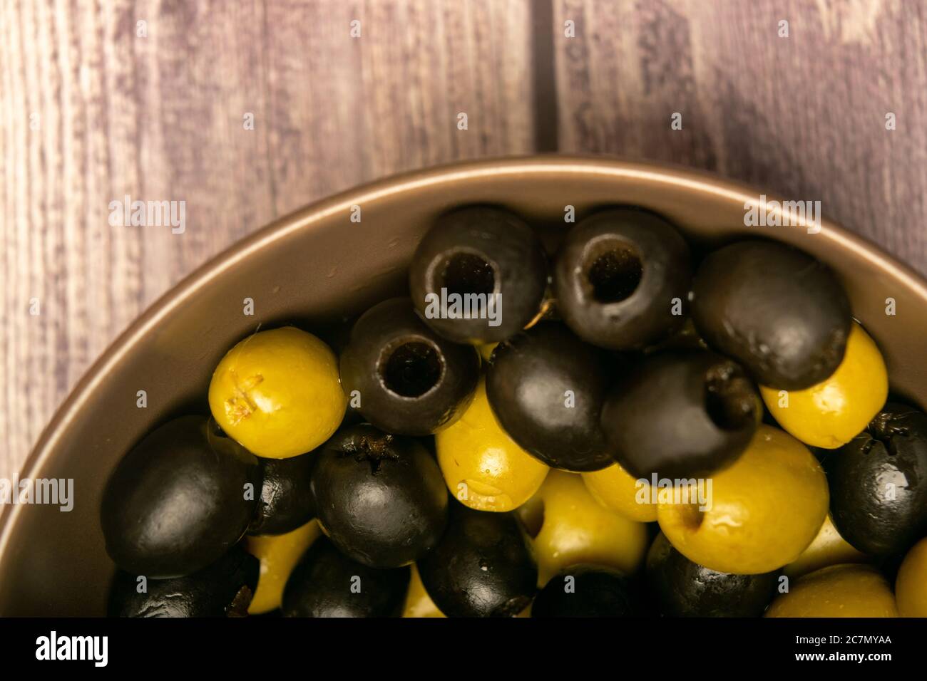 Grüne Oliven und schwarze Oliven in einer Keramikschale auf Holzgrund. Nahaufnahme Stockfoto