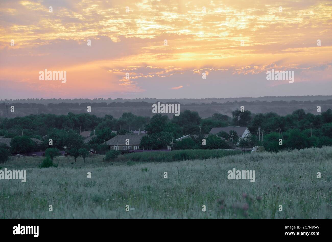 Die ländliche Landschaft im Sommer ist in den Strahlen des Sonnenuntergangs und von bewölktem Himmel beleuchtet. Stockfoto