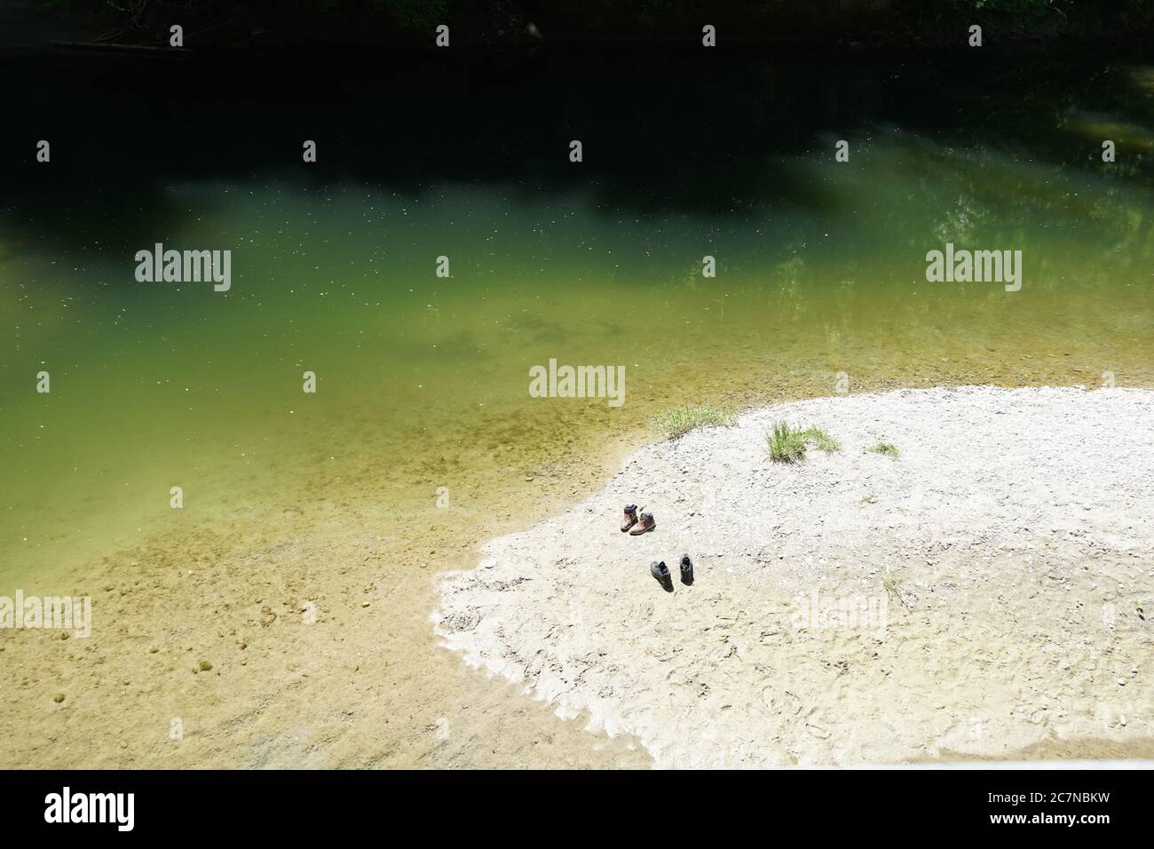 Ein kleiner Fluss nay mit Sandbänken an einem rechten Sommertag. Zwei Paar Schuhe am Ufer bedeuten, dass zwei Personen Wasser genießen. Stockfoto