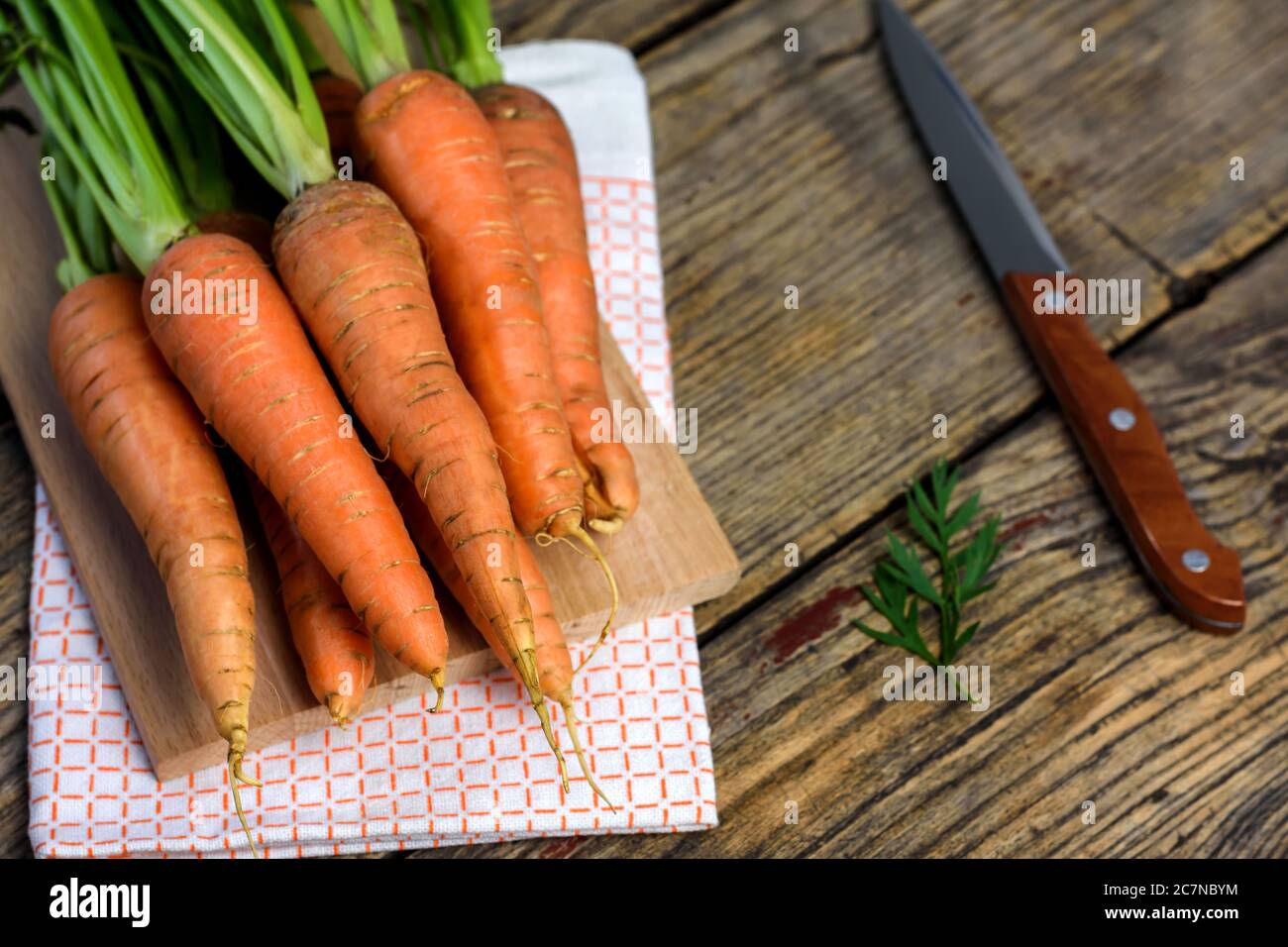 Frische Karotten auf einem Schneidebrett, Messer und Geschirrtuch auf altem Holztisch. Selektiver Fokus. Stockfoto