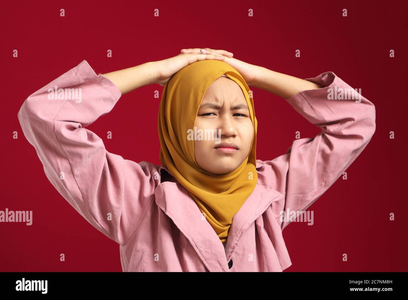 Junge muslimische Teenager-Mädchen trägt Hijab starrte auf Kamera mit verdächtigem Blick, wütend zynischen Ausdruck, vor rotem Hintergrund Stockfoto
