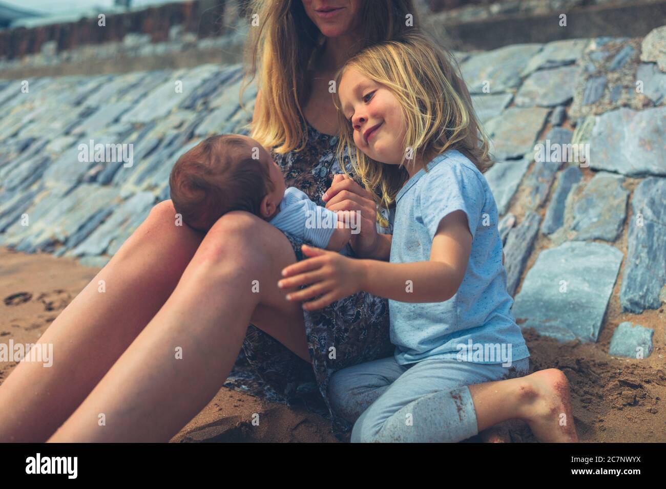 Eine junge Mutter sitzt mit ihrem Kindergartenkinder und ihrem Neugeborenen am Strand Stockfoto