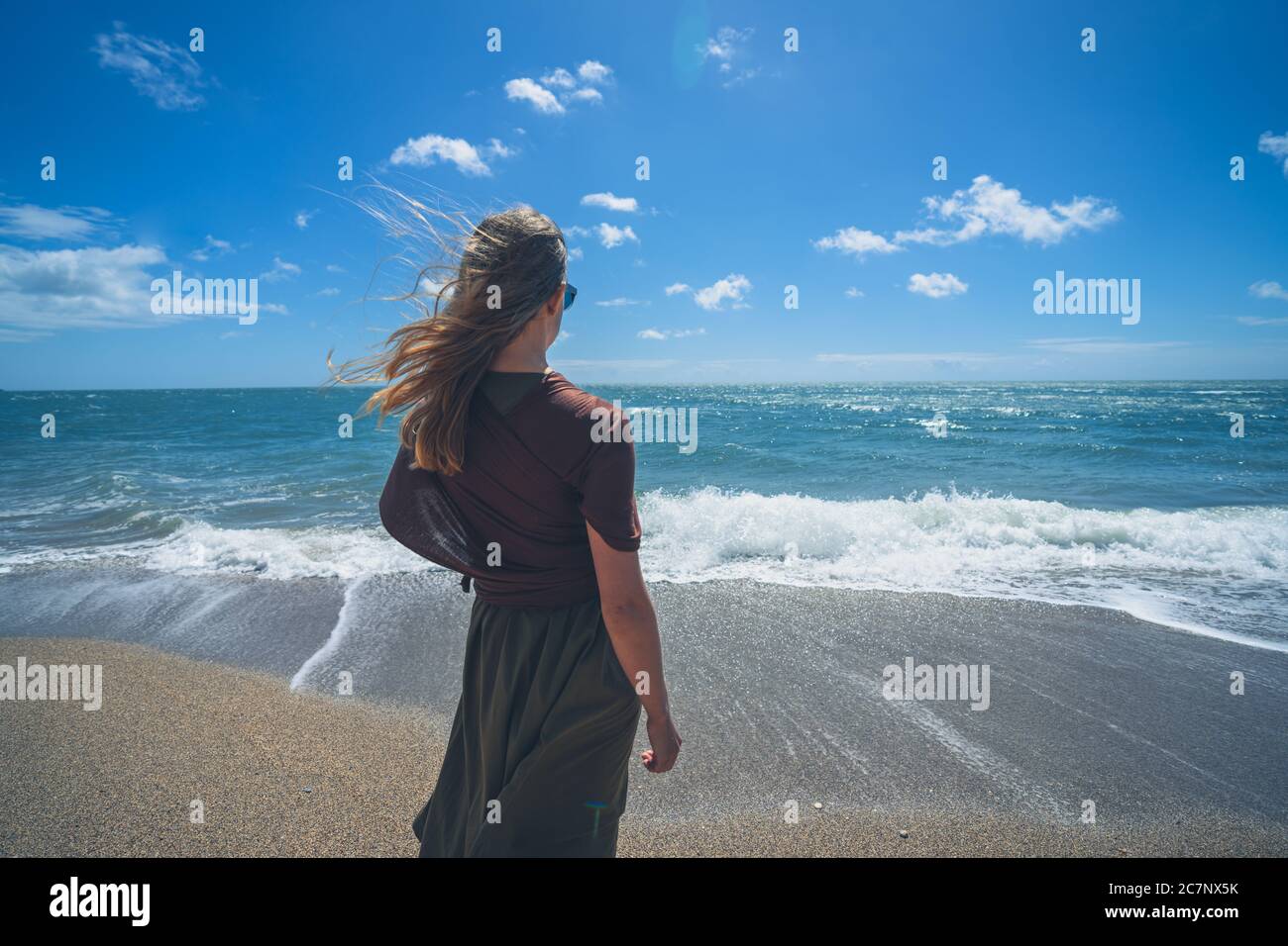 Eine junge Frau läuft am Strand, an einem sonnigen Sommertag brechen die Wellen ein Stockfoto