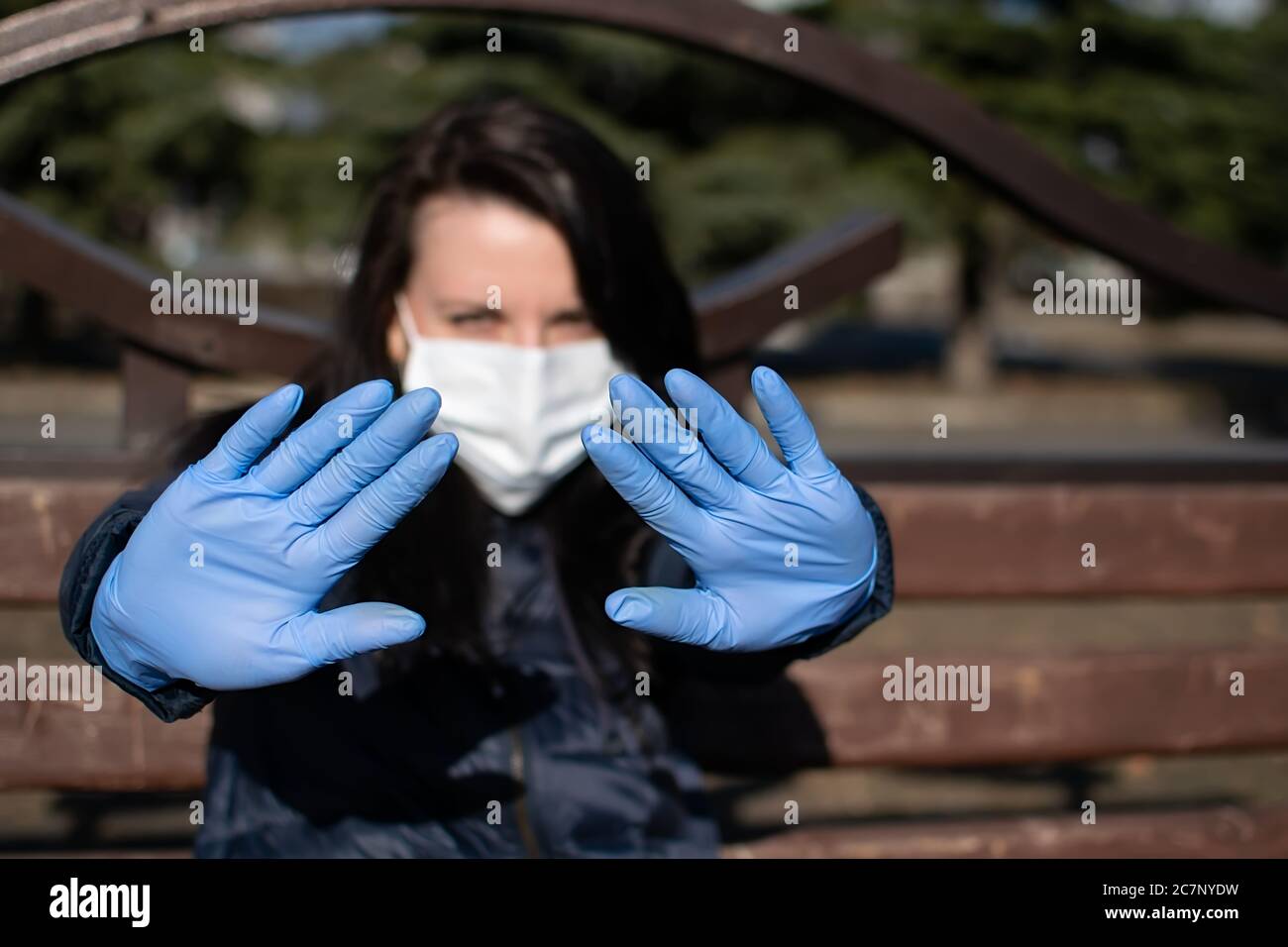 Das Mädchen, das ihre Hände in medizinischen Gummihandschuhen und einer Anti-Virus-Maske ausstreut, warnt, dass Sie Abstand von ihr halten müssen Stockfoto