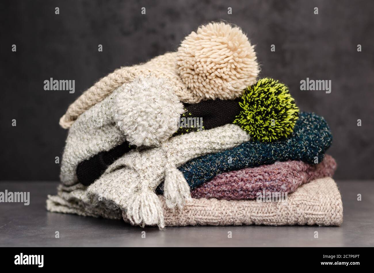 Ein Stapel gefaltetes gestricktes Winterschals und Hüte. Saison der warmen Kleidung. Zeit zum Warmhalten. Nahaufnahme Stockfoto