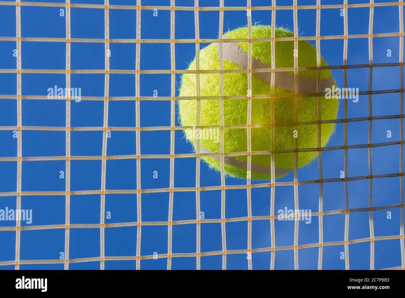 Ein gelber Tennisball, der auf den Saiten eines Tennisschlägers ruht, der von unten gegen den blauen Himmel betrachtet wird Stockfoto