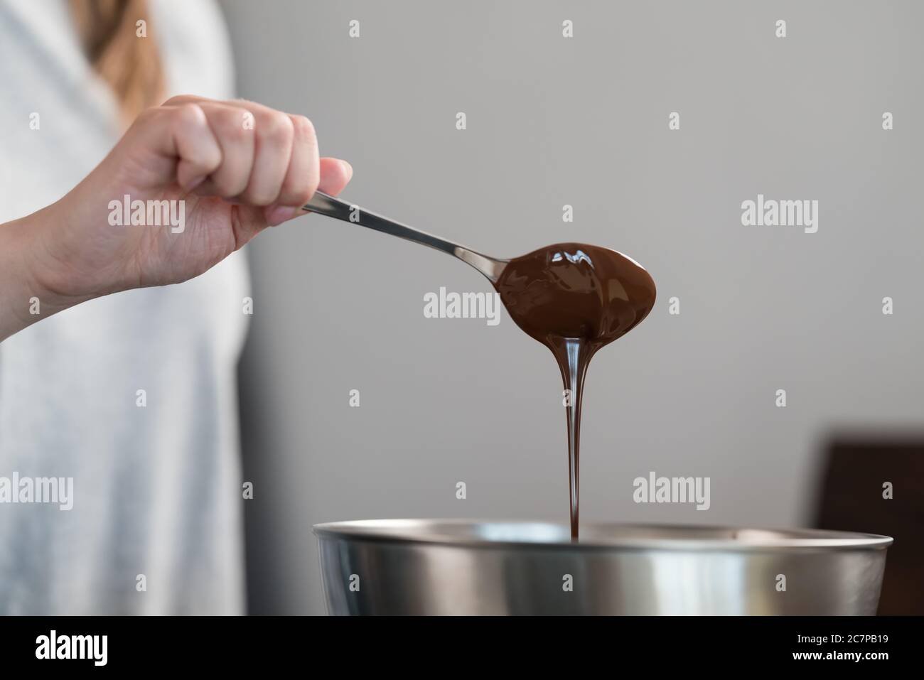 Junge Frau, die Schokolade in einer Stahlschüssel mischt, um Kerzen zu machen Stockfoto