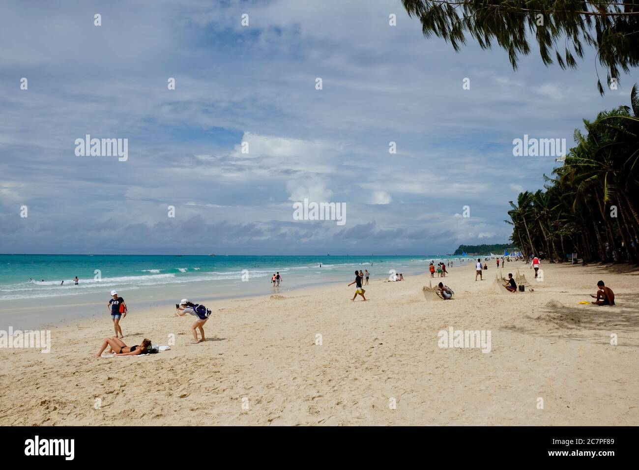 Auf Boracay Island entspannen sich Touristen an einer breiten Sandküste mit Bäumen. Prächtige weiße Wolken sonnigen Himmel. Schöner grüner Meereshorizont Stockfoto