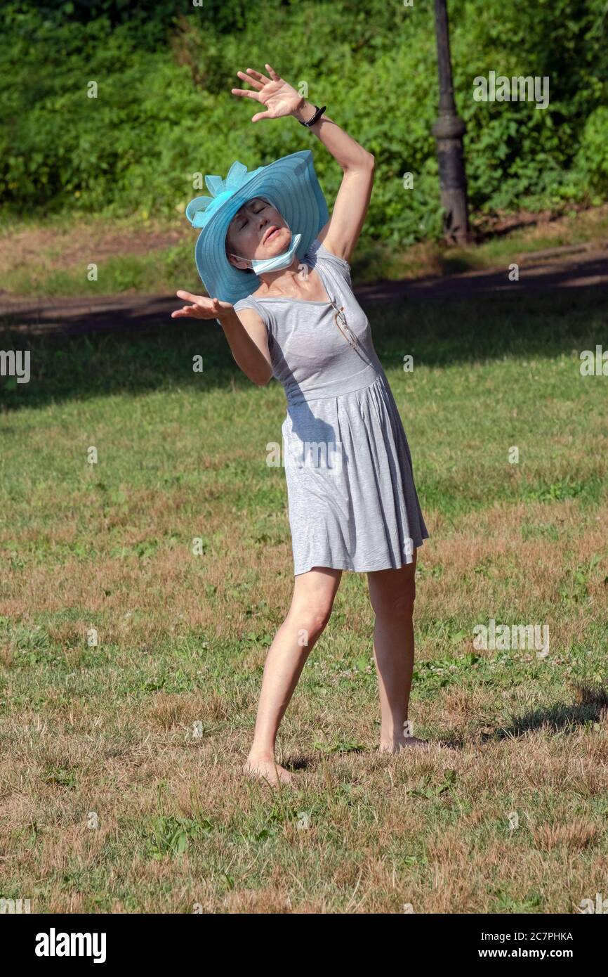 Eine asiatisch-amerikanische Frau mit ihrer Maske um den Hals tanzt in einem offenen Feld in Flushing, Queens, New York City. Stockfoto