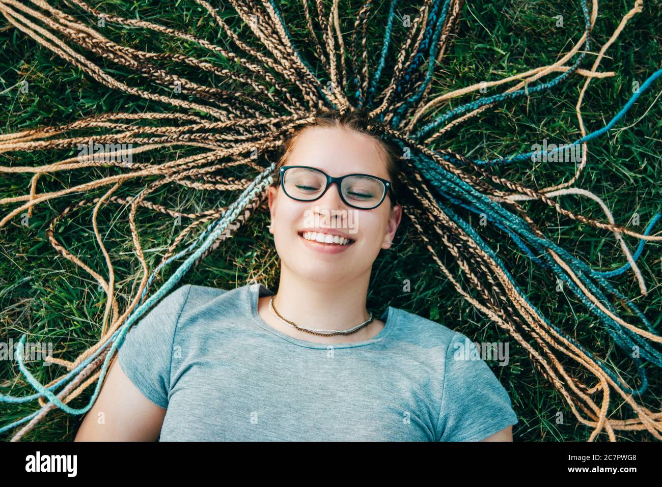 Fröhliche junge Frau trägt eine Brille liegt auf Gras. Stockfoto