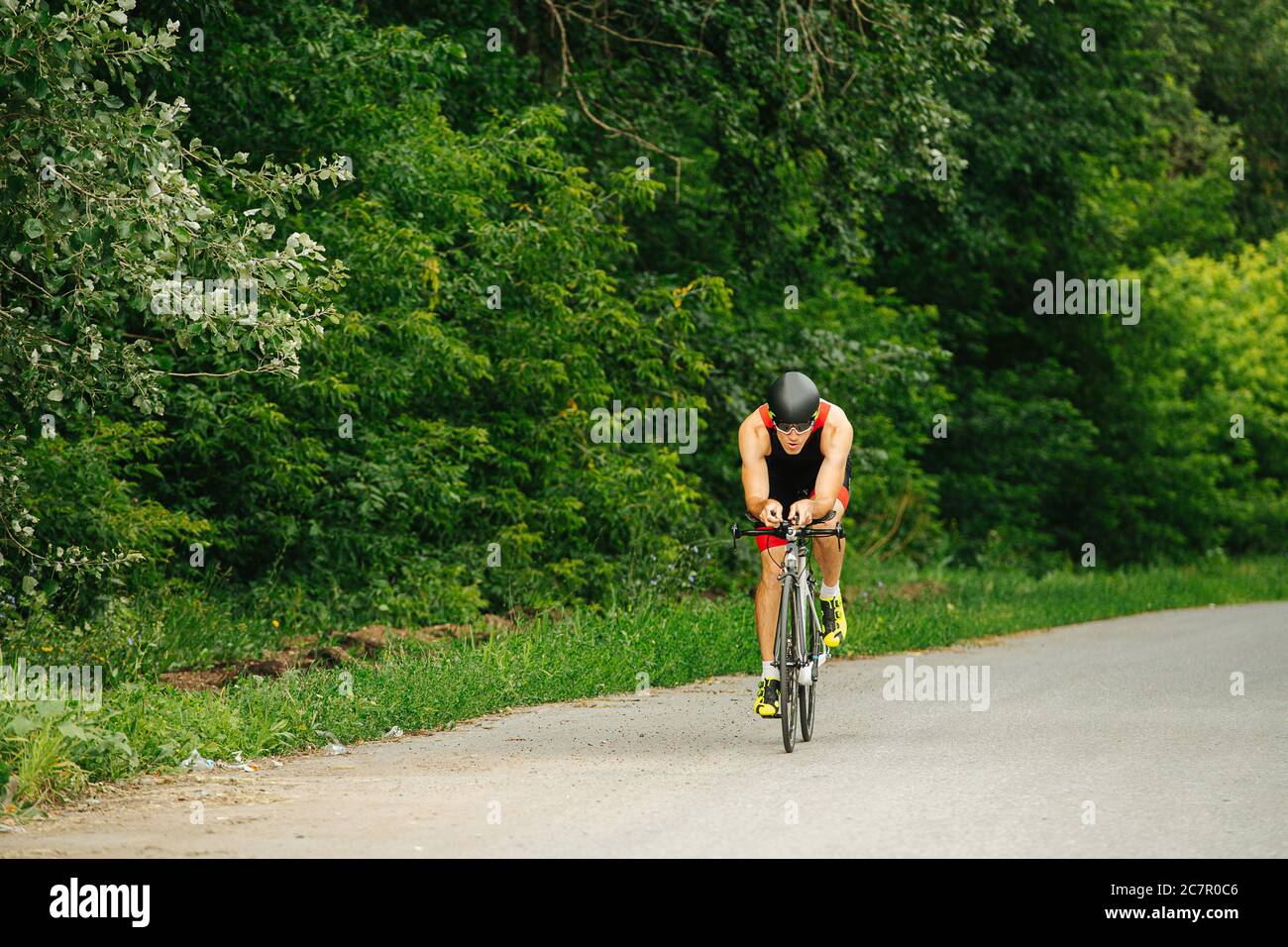 Schöner muskulöser Profi-Biker auf einer Straße mit Bäumen an den Seiten reiten Stockfoto