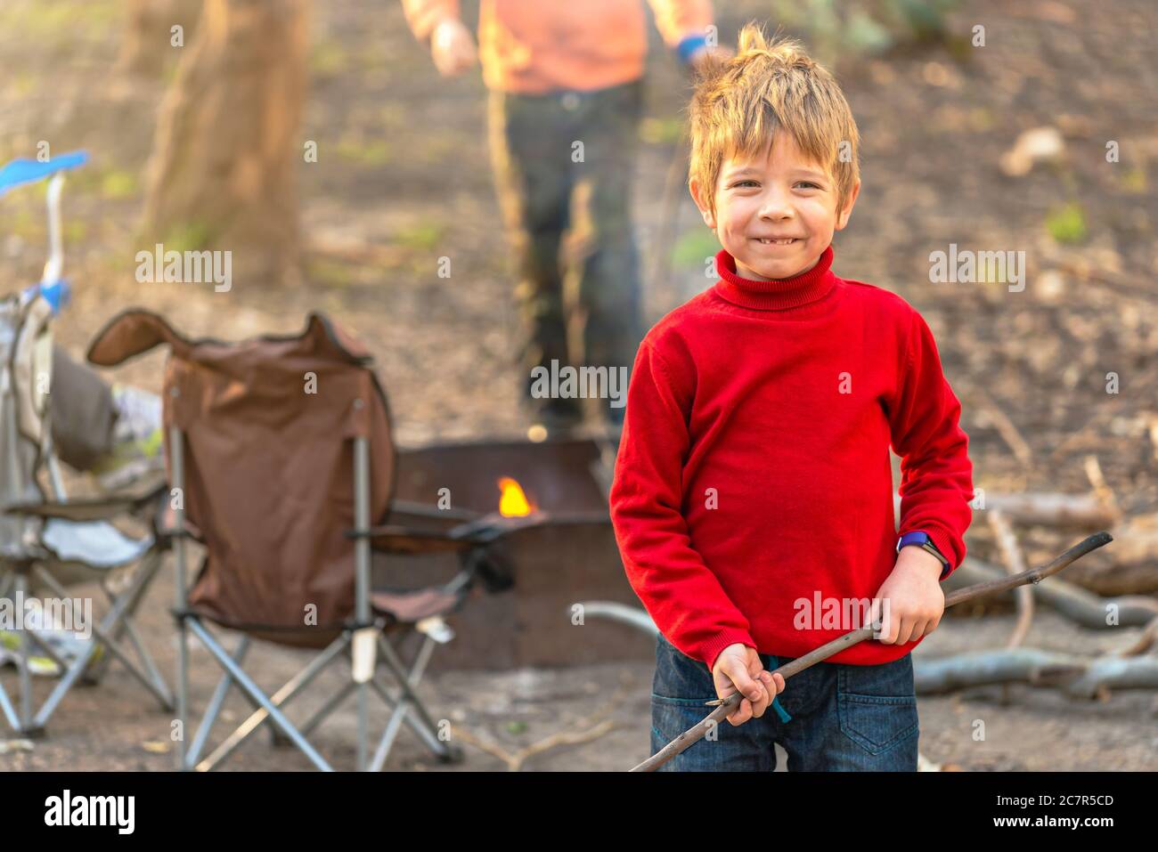 Glückliches Kind hält einen Stock, während das Feuer auf Kuitpo Wald Campingplatz während der Winterschulferien in Südaustralien brennt Stockfoto