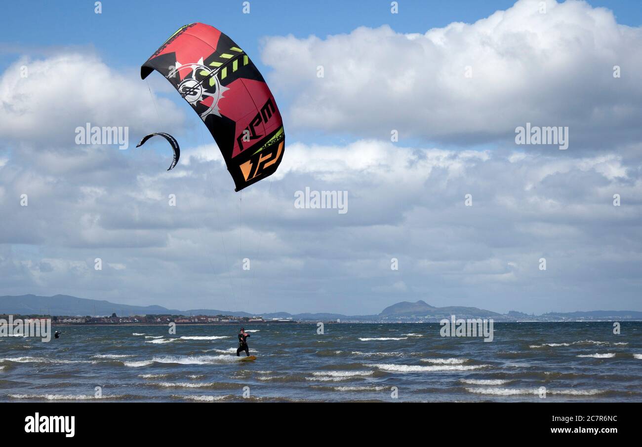 Longniddry, East Lothian, Schottland, Großbritannien. 19. Juli 2020. Im Bild: Die Kitesurferin Natalie packte 10 Minuten Wind aus westlicher Richtung, bevor die Bedingungen weniger günstig wurden und die Böen weniger geeignet waren, um den Firth of Forth zu heben, mit der Stadt Edinburgh und Arthurs Seat im Hintergrund. Temperatur von 16 Grad hell und bewölkt vor Mittag, wenn dickere Wolke zog in. Stockfoto