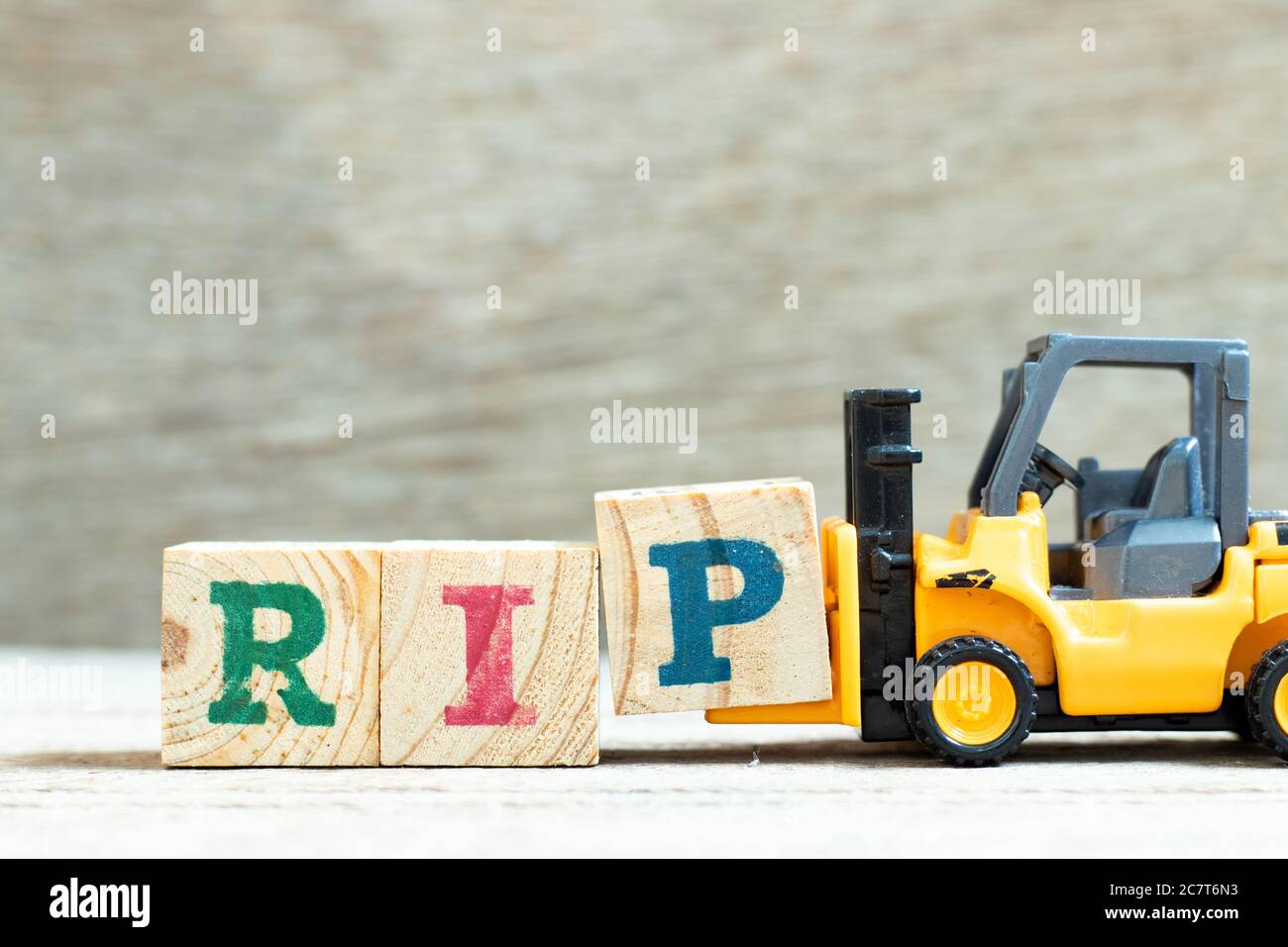 Spielzeug Gabelstapler halten Buchstabenblock P, um Wort RIP (Abkürzung für Ruhe in Frieden) auf Holzhintergrund zu vervollständigen Stockfoto