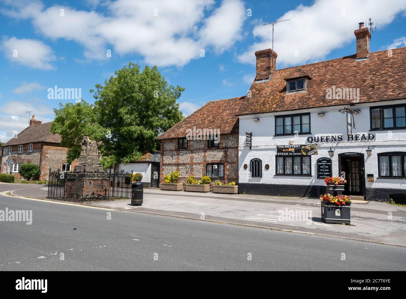 Das Queens Head Pub in der Hauptstraße von Ludgershall, einer Stadt in Wiltshire, Großbritannien, mit dem mittelalterlichen Predigerkreuz Stockfoto