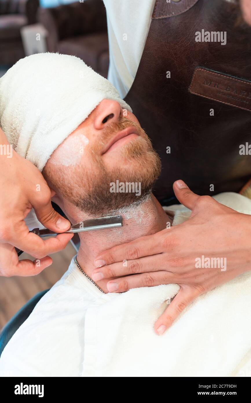 Vertikale Aufnahme eines Friseurs rasieren den Bart eines Junger Kunde in  einem Handtuch mit Klinge Stockfotografie - Alamy