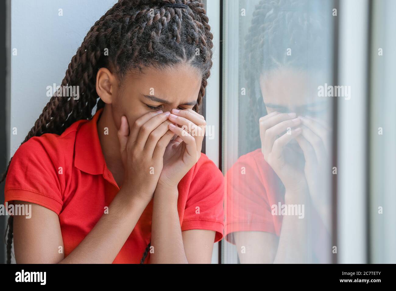 Trauriges afroamerikanisches Mädchen, das auf der Fensterbank sitzt. Stoppen Sie Rassismus Stockfoto