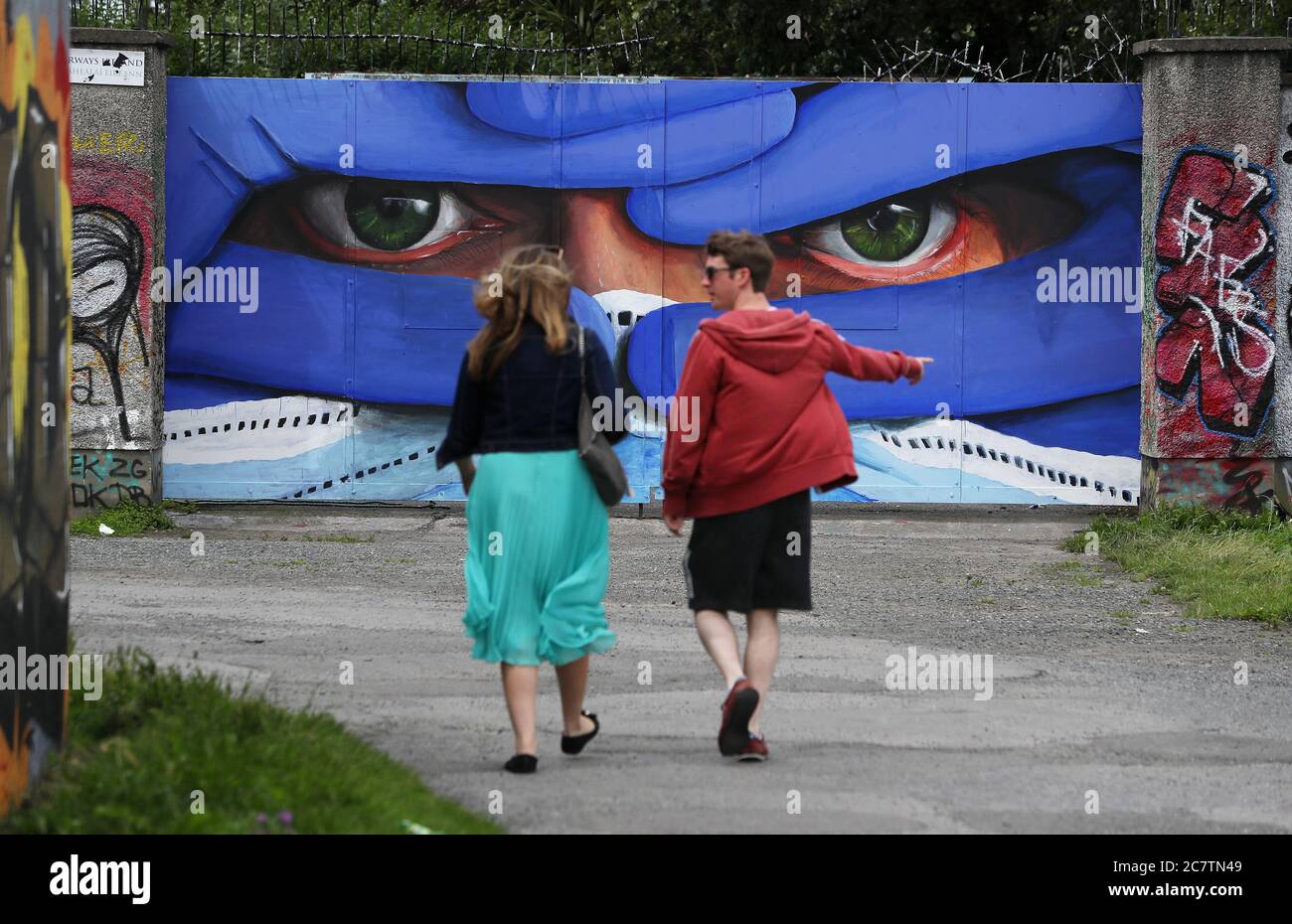 Die Menschen laufen vorbei an Dublins Künstler Asbest' neuesten in seiner Serie von Masken-Porträts, das Wandbild in Dublins Innenstadt ist mit dem Titel "Protect US" und unterstreicht die Notwendigkeit, Schutzmasken zu tragen, um die Ausbreitung von Covid-19 zu kontrollieren. Stockfoto