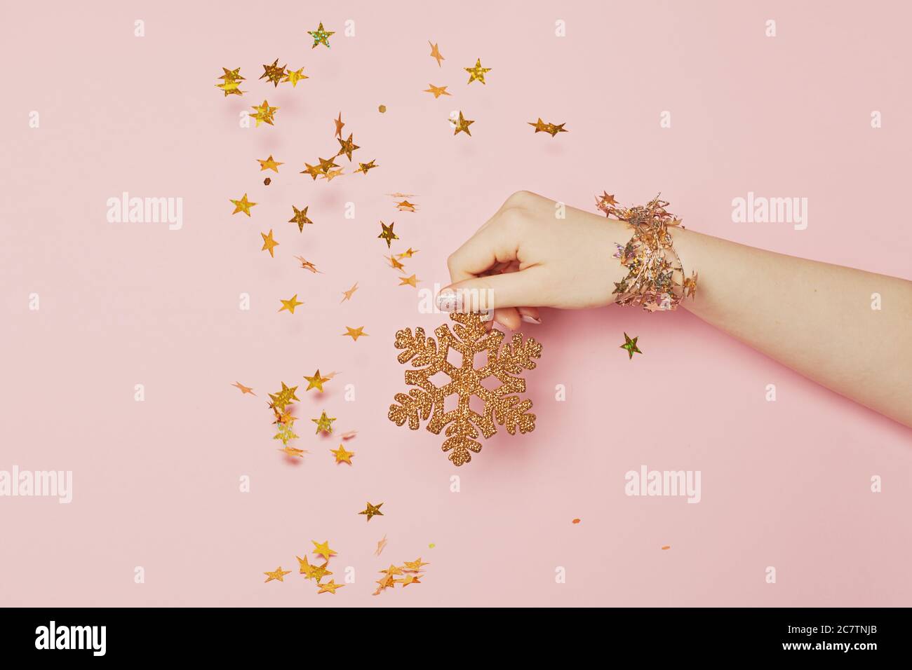Goldene Schneeflocke in weiblicher Hand und goldene Sterne auf rosa Hintergrund. Megical Weihnachtsfeiertagskonzept Stockfoto