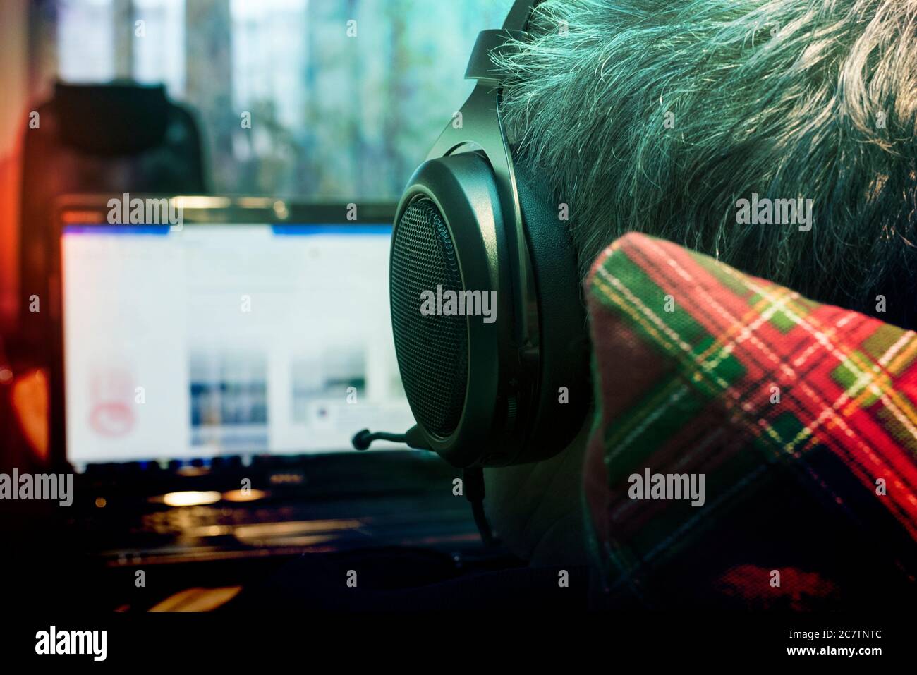 Mann mit Kopfhörer und Mikrofon, der auf dem Laptop-Monitor auf dem Kissen lag, Blick von hinten Stockfoto
