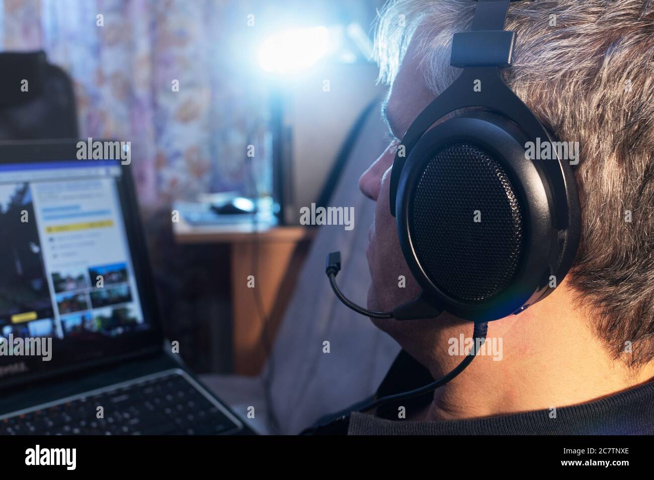 Mann mit Kopfhörer und Mikrofon, der auf den Laptop-Monitor auf dem Bett lag, Blick von hinten Stockfoto