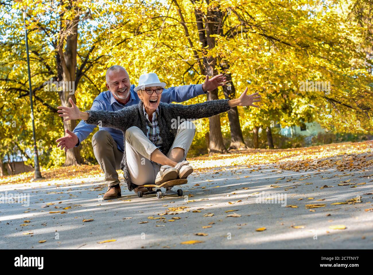 Ein älteres Paar sitzt auf einem Skateboard und hat Spaß zusammen In einem Park Stockfoto