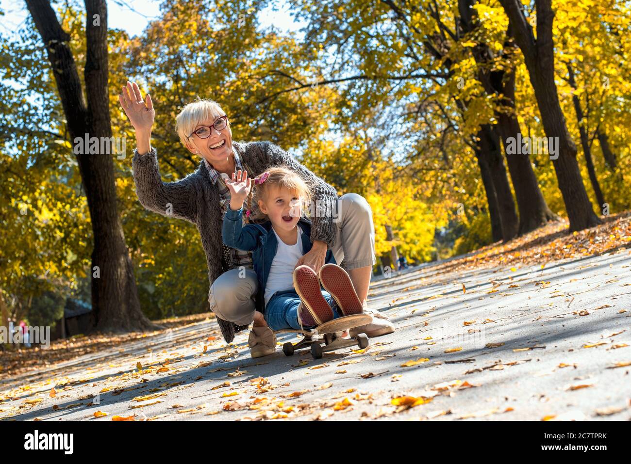 Großmutter und ihre Enkelin sitzen auf einem Skateboard und haben Spaß in einem Park Stockfoto