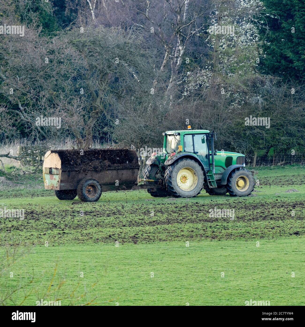 Farmer arbeiten, fahren grüne Bauernhof Traktor ziehen Seitenstreuer, Dreck (Dünger Dünger) Verbreitung auf Ackerland Weidefeld - Yorkshire, England Großbritannien Stockfoto
